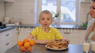 穿着黄色衬衫的蓝色大眼睛的小白种人男孩在厨房里玩得很开心。 早上好。 儿子和母亲在一起。 现代厨房